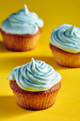 Unusual cupcakes with a beautiful blue cream. Cakes with perfect caps made from protein cream. Whipped cream with blue food color. Treat for children on a yellow-blue background.