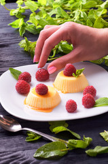 Girl decorates a delicious creamy Italian panna cotta with fresh raspberries. Woman chef prepares gourmet pudding for dessert closeup. A treat with caramel sauce.