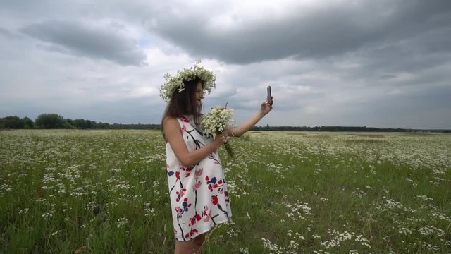 Beautiful pregnant girl doing selfie, photo with camomile flowers outside.