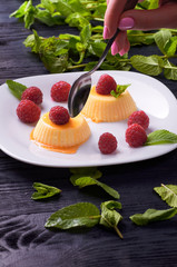The girl is going to eat delicious panna cotta with caramel sauce small teaspoon. A woman wants to lose weight and eats a dietary dessert. Delicious Italian pudding with fresh mint and raspberries.
