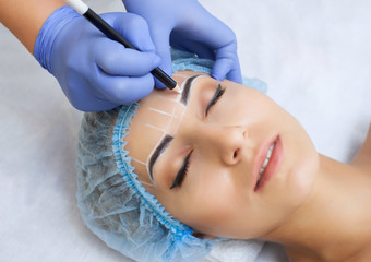 Permanent make-up for eyebrows of beautiful woman with thick brows in beauty salon.  beautician...