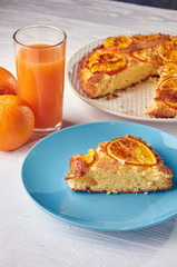 Lush biscuit with orange candied fruit. Oranges and freshly squeezed juice from them on a snow-white wooden table. Typical breakfast on weekends.