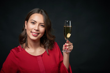 Closeup portrait of sensual brunette woman holding a glass of champagne, over dark background