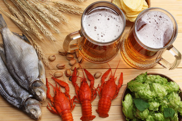 Glass beer with crawfish, hop cones and wheat ears on light wooden background. Beer brewery...