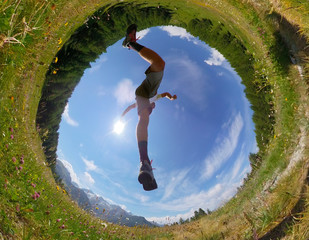 Man makes a jump in a mountain meadow. View from below. Daylight, summer season, fisheye lens.