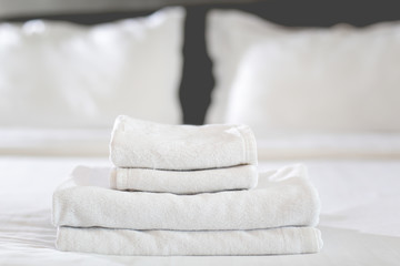 Close-up of hands putting stack of fresh white bath towels on the bed sheet. Room service maid cleaning hotel room.