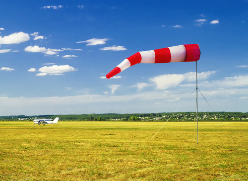 red and white windsock wind sock on blue sky on the aerodrome, yellow field and clouds background