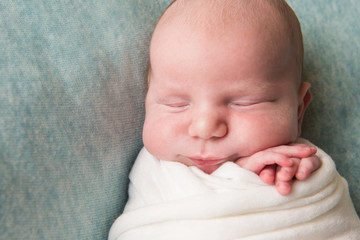 smiling newborn baby folded his arms close-up. Top view