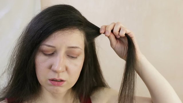 A woman holds a strand of her hair. The girl has symptoms of crisis: a feeling of lack of air, rapid heartbeat. Close-up, indoor, real-time