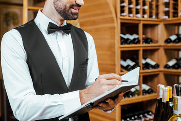 cropped shot of smiling young wine steward making notes at wine store