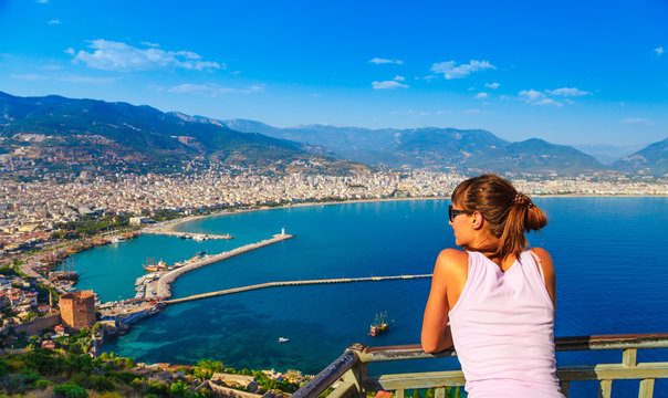 Woman look on landscape of Alanya with marina and Kizil Kule red tower in Antalya district, Turkey, Asia. Famous tourist destination with high mountains. Summer bright day and sea shore