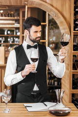 confident young sommelier examining color of wine at wine store