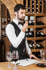 handsome young wine steward examining aromatic bottle corc after opening wine at store