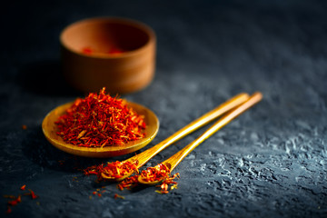Saffron spices. Saffron on black stone table in a wood bowl and a spoon. Spice and herbs on slate...