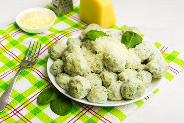 Big plate with spinach gnocchi on green tissue  with cheese