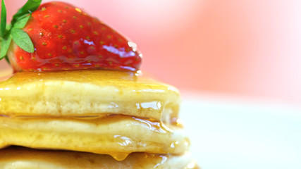 Stack of pancakes with strawberry on top and drizzled with syrup, macro closeup.