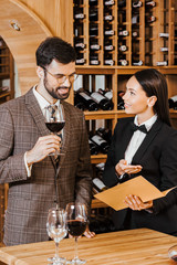 Female wine steward showing menu list to client at wine store