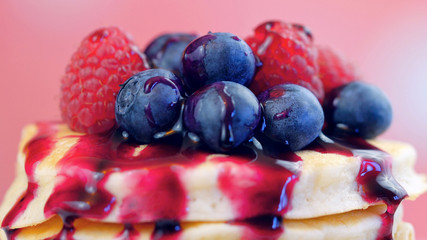 Stack of pancakes with raspberries, blueberries and drizzled with blueberry maple syrup, macro closeup.