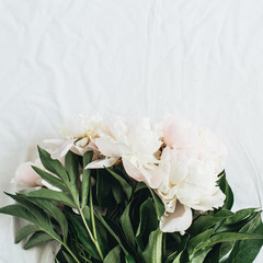 Flat lay, top view of white peonies flower bouquet on white blanket background.