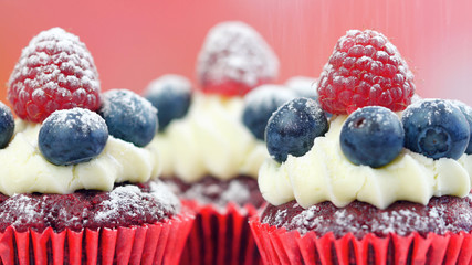 Macro closeup of red velvet cupcakes decorated with fruit and dusting with confectionery sugar.