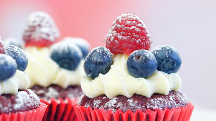 Macro closeup of red velvet cupcakes decorated with fruit and dusting with confectionery sugar.