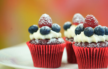 Macro closeup of red velvet cupcakes decorated with fruit and dusting with confectionery sugar.