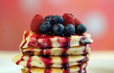 Stack of pancakes with raspberries, blueberries and drizzled with blueberry maple syrup, macro closeup.