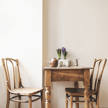 Vintage Interior Design Of Kitchen Space With Small Table Against White Wall With Simple Chairs And Plant Decorations. Minimalistic Concept Of Kitchen Space.