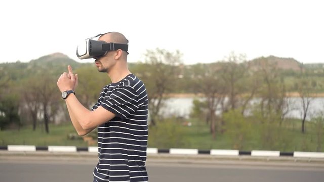 A young man stands in front of nature in a virtual reality helmet.Dive games or panoramic video - the movie that goes around it, and looking around as in life. The world of virtual reality