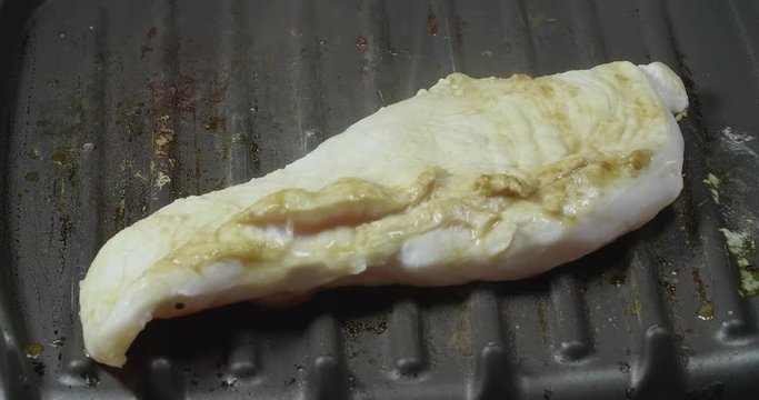 close up of a chicken being grilled while letting out smoke in a grill surrounded by grease looking delicious 