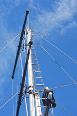 Obraz premium The mast of yacht rising against a blue sky. A ladder and rope rigging run alongside the mast.