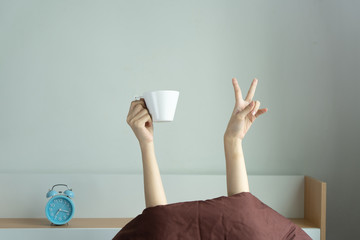 Woman showing funny v sign holding blue tea cup relaxing in bed room, Young woman with two hands...