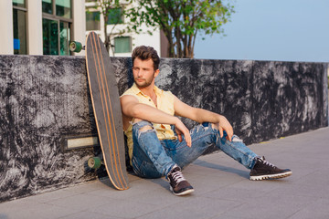 Young man sitting with longboard on the street.
