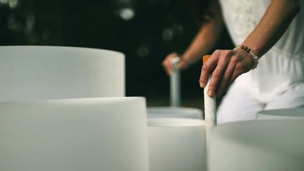A woman's hands playing two crystal bowls at the same time in golden morning light shot on a slider moving backwards shot in slow motion.