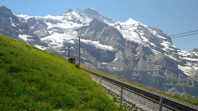 Static shot of a red train carrying tourists downhill from the Jungfrau Mountain range toward Kleine Scheidegg