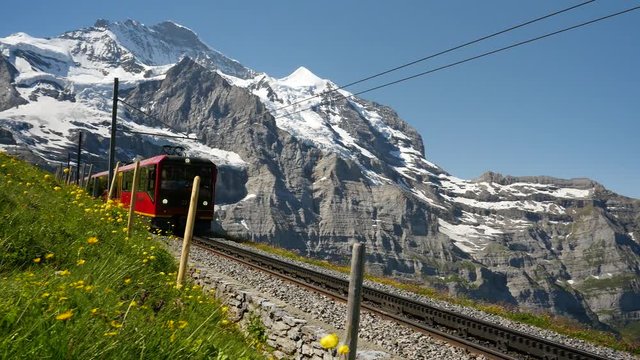 Jib shot of a red train carrying tourists downhill from the Jungfrau Mountain range toward Kleine Scheidegg