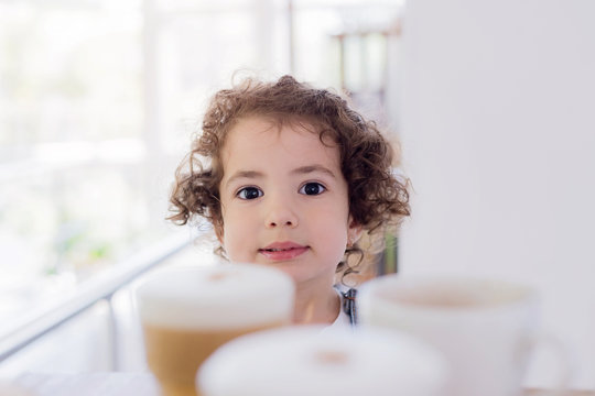 Little girl is sitting at the table whith cups of coffee and cappucino