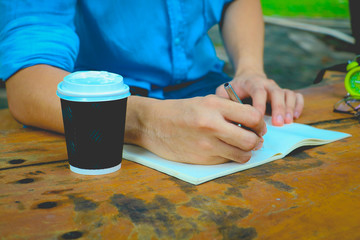 Obraz premium In the morning . Men sitting in the park and he writing notebook. He drinking coffee and working on idea on notebook in relax time .
