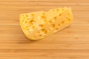 Piece of Swiss-type cheese on bamboo cutting board