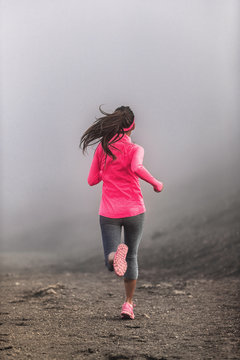 Run fit woman runner running on trail path in mountains in fog and clouds - morning jogging training in pink sportswear clothes.
