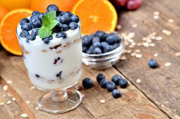Yogurt with oatmeal, fresh blueberries and mint leaves and orange and grapes in background