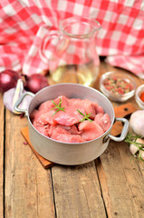 Raw pork meal diced in a bowl, garlic, half of onion, pepper, jug with oil and checkered red tablecloth in the background - vertical photo