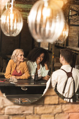 Nice conversation. Cheerful young women talking to barman and smiling at him while drinking beer in the bar
