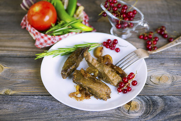 Fried liver with onions and vegetables on a wooden background