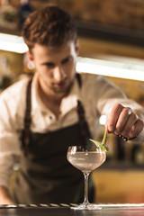Sweet decoration. Handsome young barman adding decoration on the glass with a cocktail being in the focus