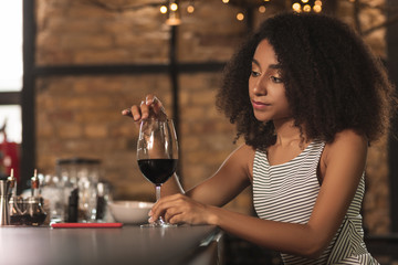 Relaxing in bar. Beautiful young woman touching the rim of a glass of a red wine with her finger while sitting in the bar