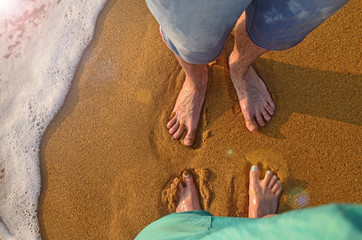 Two pairs of feet stand on the sand and wait for the wave to come. wave on the sandy beach of...