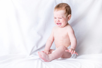 Cute baby 6-9 months old sad crying white background. Children's emotions. The pain of teething