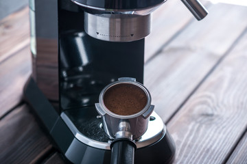 Preparation of espresso. Black coffee machine and a horn with ground grains on the table. Professional coffee brewing