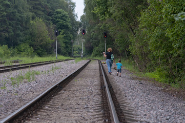 A woman with a child walks along a railway in the forest